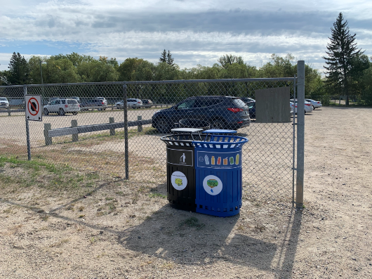 Recycle and garbage bin in field near parking lot